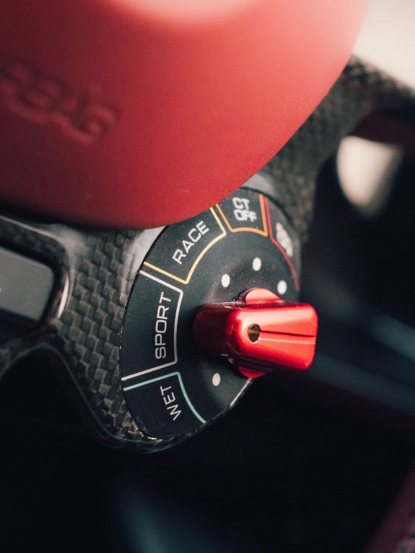Ferrari drive mode selector showing WET, SPORT, RACE, CT OFF on red carbon steering wheel
