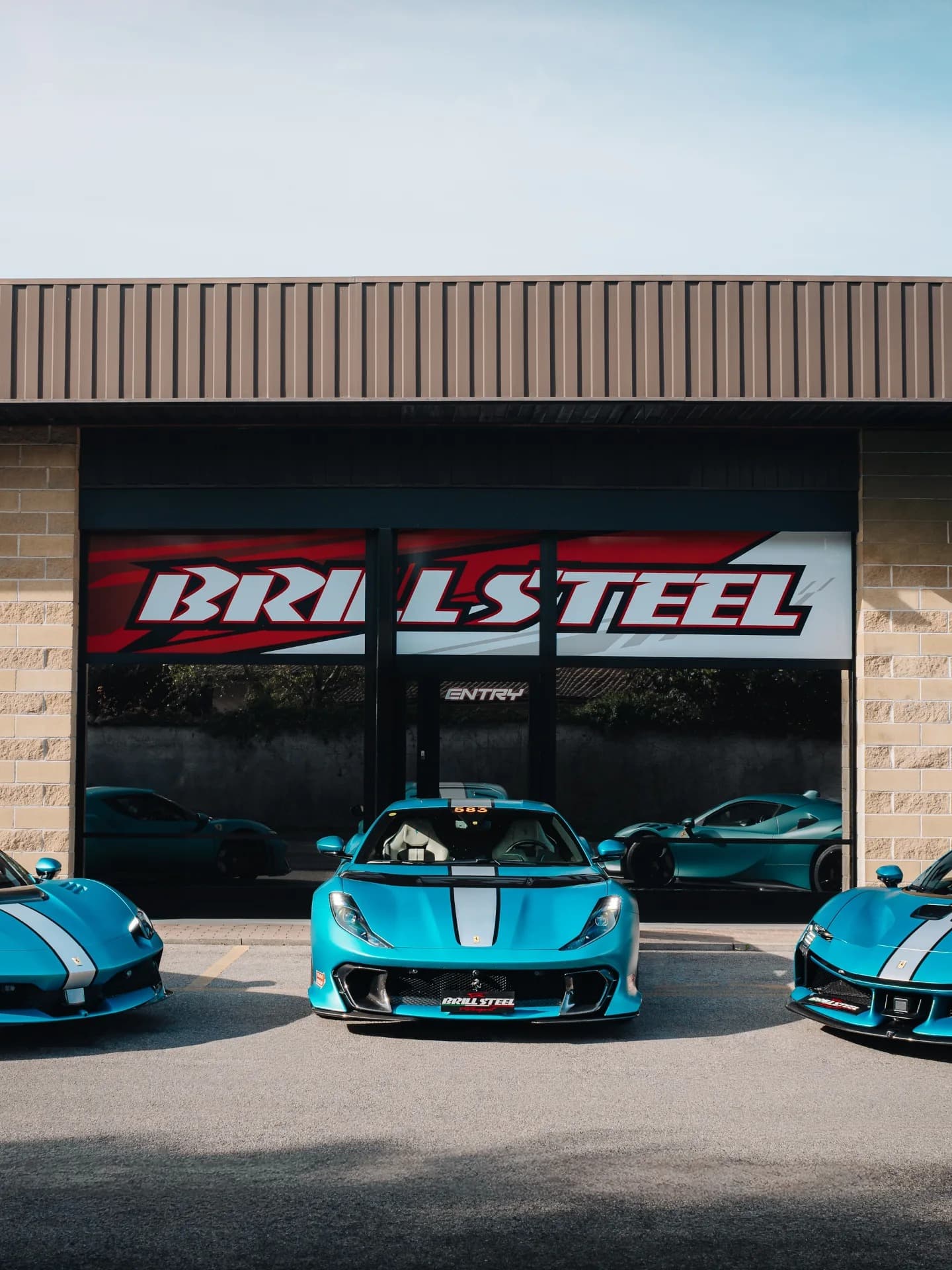 Three Brill-Steel Ferraris in matte teal — 812 Competizione, 296 GTB, SF90 Stradale — in front of the Italian workshop